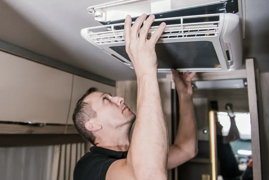 Service technician inspecting the ceiling air conditioning vent inside a RV