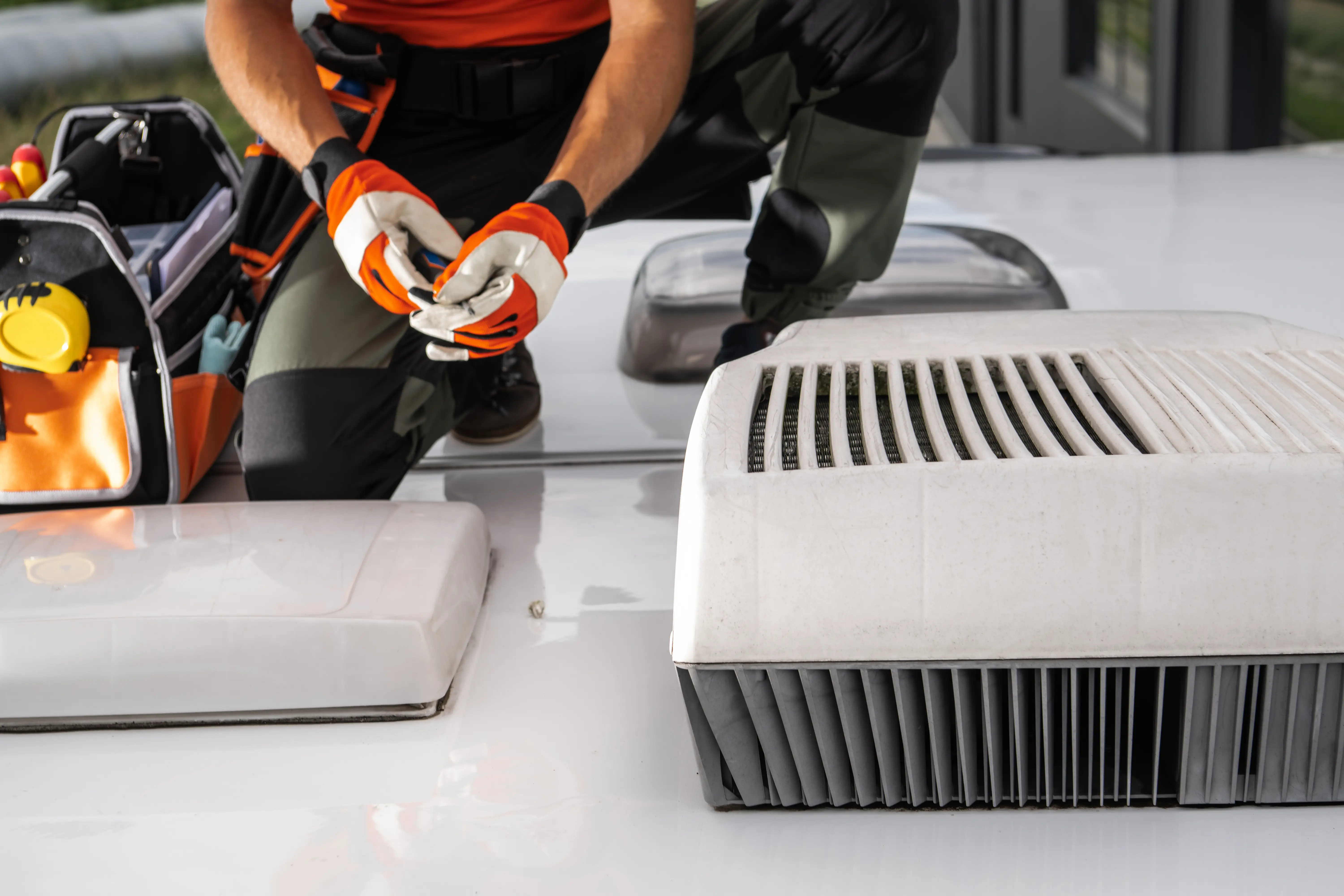 Service technician working on a white rooftop air conditioning unit on an RV