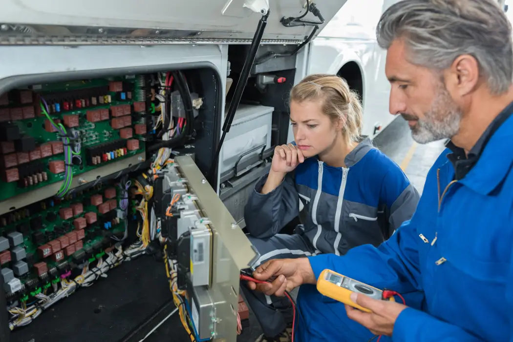 Two service technicians inspecting and testing an electrical control panel inside RV.